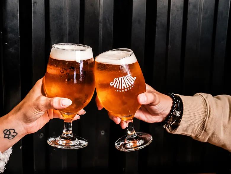 Dos personas brindando con cerveza tirada frente a la pared del local.