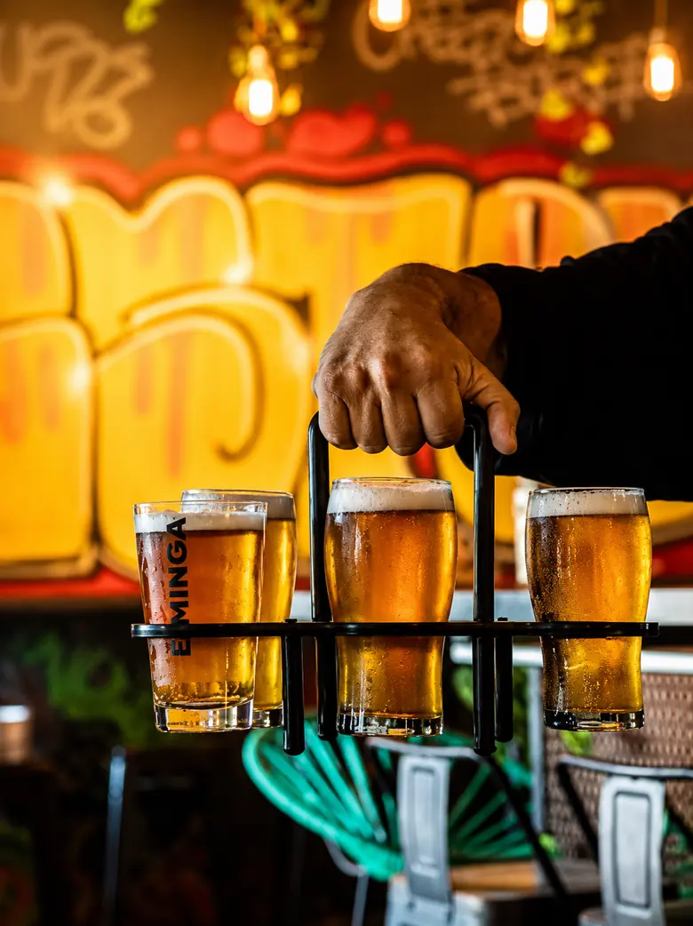 Bandeja con seis vasos de cerveza tirada frente a un mural del local.