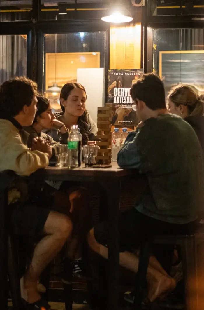 Una mesa alta junto a la ventana, con varias personas alrededor y una torre de maderitas en el medio.